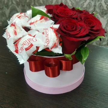 Доставка на ефектна композиция от червени рози и зеленина, аранжирани в красива кутия за цветя и 10 бонбона Raffaello, прикрепени към тях.